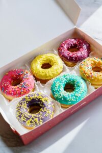 Brightly colored glazed donuts with sprinkles in a box, captured on a marble background, showcasing their vibrant colors.